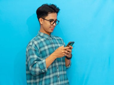 Mavi tişörtlü gülümseyen Asyalı adam elinde mavi arka planı olan bir akıllı telefon tutuyor. Teknoloji, yaşam tarzı ya da reklam kavramları için mükemmel..