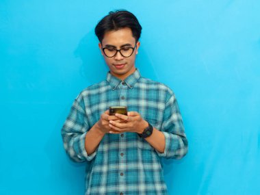 Mavi tişörtlü gülümseyen Asyalı adam elinde mavi arka planı olan bir akıllı telefon tutuyor. Teknoloji, yaşam tarzı ya da reklam kavramları için mükemmel..