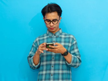 Mavi tişörtlü gülümseyen Asyalı adam elinde mavi arka planı olan bir akıllı telefon tutuyor. Teknoloji, yaşam tarzı ya da reklam kavramları için mükemmel..