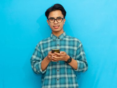 Mavi tişörtlü gülümseyen Asyalı adam elinde mavi arka planı olan bir akıllı telefon tutuyor. Teknoloji, yaşam tarzı ya da reklam kavramları için mükemmel..