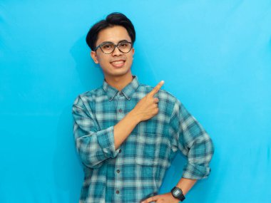 Mavi tişörtlü gülümseyen Asyalı adam mavi arka planı işaret ederek pozitifliği ve dostça iletişimi ifade ediyor..