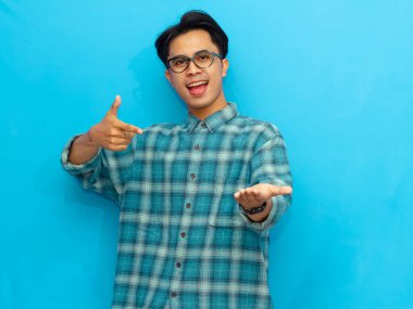 Mavi günlük gömlekli mutlu Asyalı adam, mavi bir arka planda soyutlanmış, neşeli bir ifadeyle avucuna bakıyor..