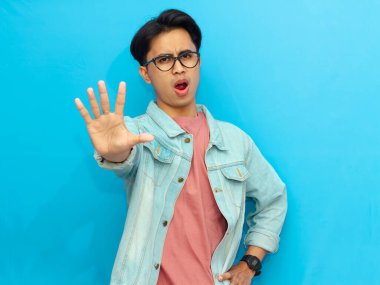 Kot ceketli kızgın bir Asyalı, mavi arka planda tek başına elini hareket ettiriyor..