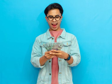 Kot ceketli genç Asyalı adam elinde nakit para tutuyordu. Elinde tuttuğu paranın mavi arka planda izole edilmesine şaşırmıştı..