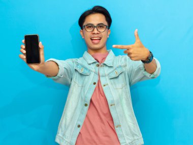 Heyecanlı Asyalı genç adam boş akıllı telefon ekranını işaret ediyor, mavi arka planda izole edilmiş. Mobil bir uygulama, teklif ya da reklam konsepti sunuyorum. Pazarlama ve reklam kullanımı için mükemmel.