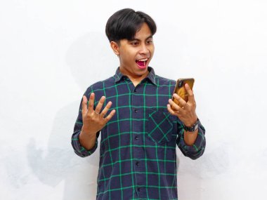 Akıllı telefon tutan yakışıklı bir Asyalı adamın portresi ve beyaz bir arkaplanda izole edilmiş, hayret verici bir ifadeyle ona bakıyor. Reklam ve promosyon için mükemmel..