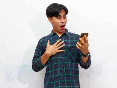 Akıllı telefon tutan yakışıklı bir Asyalı adamın portresi ve beyaz bir arkaplanda izole edilmiş, hayret verici bir ifadeyle ona bakıyor. Reklam ve promosyon için mükemmel..