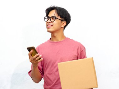 Pembe tişörtlü genç bir Asyalı 'nın portresi, gülümsüyor ve elinde cep telefonu ve beyaz bir arka planda izole edilmiş bir paket kutusu var..
