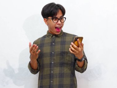 Akıllı telefon tutan yakışıklı bir Asyalı adamın portresi ve beyaz bir arkaplanda izole edilmiş, hayret verici bir ifadeyle ona bakıyor. Reklam ve promosyon için mükemmel..