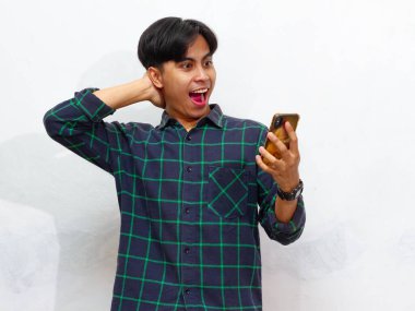 Akıllı telefon tutan yakışıklı bir Asyalı adamın portresi ve beyaz bir arkaplanda izole edilmiş, hayret verici bir ifadeyle ona bakıyor. Reklam ve promosyon için mükemmel..