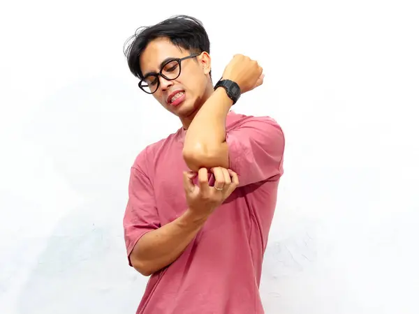 stock image Portrait of a young Asian male in a pink t-shirt, scratching his arm and body with an itchy gesture, isolated on a white background.