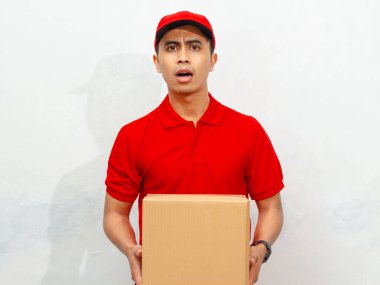 Kırmızı üniformalı ve şapkalı Asyalı erkek kurye, beyaz izole edilmiş arka planda sürpriz bir ifade sergiliyor..