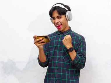 Mobil video oyunu uygulamasında akıllı telefon oyunu oynayan heyecanlı Asyalı genç oyuncu ya da beyaz arkaplanda izole edilmiş dijital video akışı cep telefonunu izleyen.