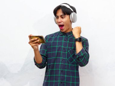 Mobil video oyunu uygulamasında akıllı telefon oyunu oynayan heyecanlı Asyalı genç oyuncu ya da beyaz arkaplanda izole edilmiş dijital video akışı cep telefonunu izleyen.