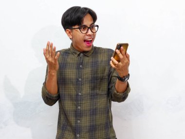 Young Asian man posing with a smartphone, showing an amazed expression against a white background. clipart