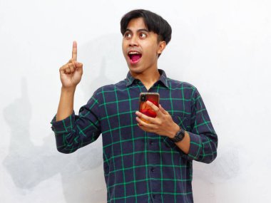 Akıllı bir telefon tutan yakışıklı bir Asyalı 'nın portresi yukarı doğru işaret ediyor ve beyaz bir arka planda izole edilmiş heyecanlı bir ifadeyle bir fikir edinme hareketi yapıyor..