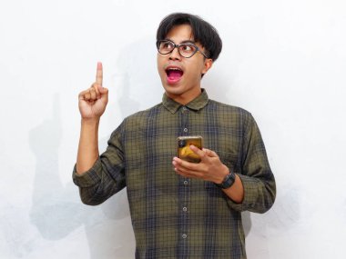 Akıllı bir telefon tutan yakışıklı bir Asyalı 'nın portresi yukarı doğru işaret ediyor ve beyaz bir arka planda izole edilmiş heyecanlı bir ifadeyle bir fikir edinme hareketi yapıyor..