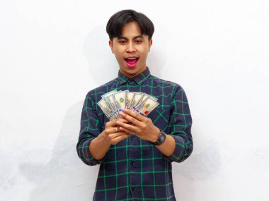 Yakışıklı Asyalı genç adam heyecanlı bir şekilde paraya bakıyor, beyaz bir arka planda izole edilmiş..