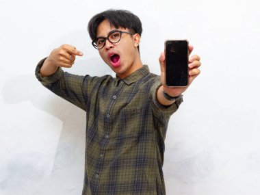 Sıradan tişörtler giyen mutlu genç Asyalı adam portresi boş ekranın akıllı telefon modelini gösteriyor ve işaret ediyor..