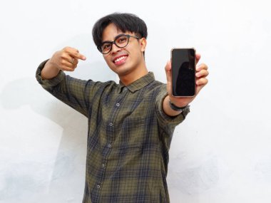Sıradan tişörtler giyen mutlu genç Asyalı adam portresi boş ekranın akıllı telefon modelini gösteriyor ve işaret ediyor..