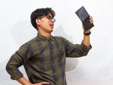 Beyaz arka planda üzgün ve komik bir ifadeyle boş bir cüzdan taşıyan fakir bir Asyalı adamın portresi..