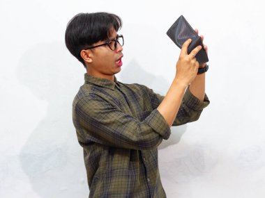 Beyaz arka planda üzgün ve komik bir ifadeyle boş bir cüzdan taşıyan fakir bir Asyalı adamın portresi..