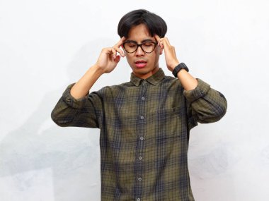 Üzgün ve üzgün bir ifadeyle genç Asyalı adam alnına dokunuyor, beyaz bir arka planda soyutlanmış..