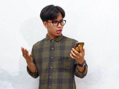 Kafası karışmış ve şok olmuş yakışıklı Asyalı bir adam elinde akıllı bir telefonla kameraya şaşırmış bir ifadeyle bakıyor. Beyaz bir arka planda izole edilmiş, reklam amaçlı mükemmel..