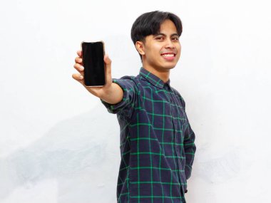 Gülümserken boş bir akıllı telefon ekranı gösteren mutlu bir Asyalı adamın portresi. Adam rahat bir gömlek giyiyor, beyaz bir arkaplanda izole edilmiş, reklam için mükemmel..