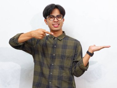 Mutlu genç Asyalı adam beyaz bir arka planda neşeli bir ifadeyle avucunu gösteriyor, heyecan ve coşku gösteriyor.