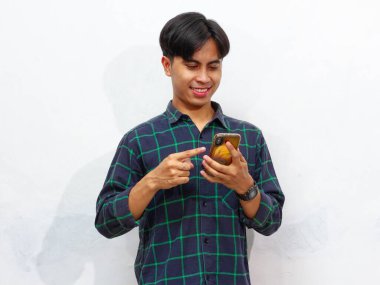 Beyaz arka planda akıllı bir telefona bakıp gülümseyen yakışıklı bir Asyalı adamın portresi. Reklam, teknoloji ve modern yaşam tarzı kavramları için mükemmel..