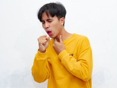 Sağlıksız Asyalı bir adamın portresi, üzgün bir ifadeyle acı içinde öksürüyor, beyaz bir arka planda izole edilmiş. Sağlık kampanyaları, reklamlar ya da tıbbi makaleler için mükemmel..