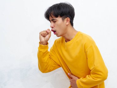 Sağlıksız Asyalı bir adamın portresi, üzgün bir ifadeyle acı içinde öksürüyor, beyaz bir arka planda izole edilmiş. Sağlık kampanyaları, reklamlar ya da tıbbi makaleler için mükemmel..