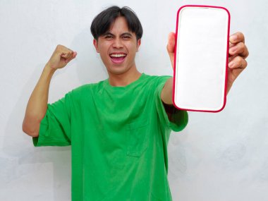 Mutlu Asyalı genç adam beyaz arka planda boş ekranlı akıllı telefon gösteriyor.