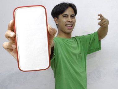 Mutlu Asyalı genç adam beyaz arka planda boş ekranlı akıllı telefon gösteriyor.