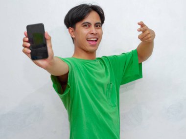 Mutlu Asyalı genç adam beyaz arka planda boş ekranlı akıllı telefon gösteriyor.