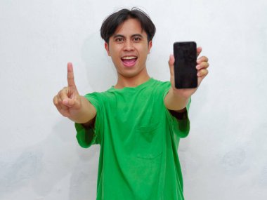 Mutlu Asyalı genç adam beyaz arka planda boş ekranlı akıllı telefon gösteriyor.