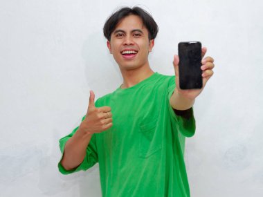 Mutlu Asyalı genç adam beyaz arka planda boş ekranlı akıllı telefon gösteriyor.