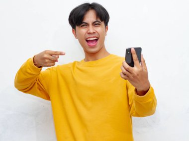 Akıllı telefonu tutan ve ona bakan heyecanlı genç adam zafer jesti yapıyor, pozitifliğini dile getiriyor ve kutluyor.