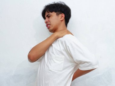 Belini ve sırtını tutan sağlıksız bir Asyalı adamın portresi rahatsızlıktan dolayı acı veren bir ifade sergiliyor. Beyaz bir arka planda izole edilmiş, sağlıkla ilgili içerik veya tıbbi reklamlar için mükemmel.