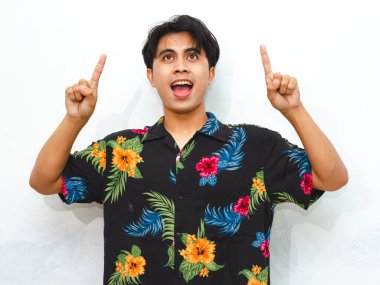 Portrait of a happy young Asian man in casual summer attire, pointing upwards to present an advertisement with enthusiasm. clipart