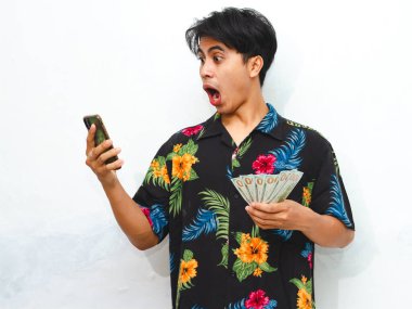 Şok olmuş bir ifadeyle akıllı telefonuna bakarken elinde para tutan sıradan yaz kıyafetleri içindeki Asyalı genç adam şaşırdı..