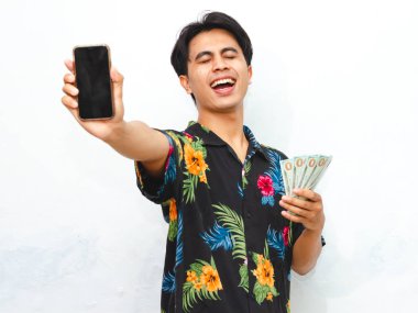 Yazın giyinmiş mutlu bir Asyalı, elinde para tutarken temiz beyaz bir arkaplana gülümseyen boş bir cep telefonu ekranı gösteriyor..