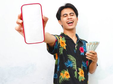 Yazın giyinmiş mutlu bir Asyalı, elinde para tutarken temiz beyaz bir arkaplana gülümseyen boş bir cep telefonu ekranı gösteriyor..