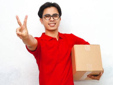 Kırmızı üniformalı, gülümseyen, kendine güveni tam bir Asyalı teslimatçının portresi. Elinde bir paket var ve beyaz arka planda iki parmağını gösteriyor. Teslimat veya kurye kavramları için ideal.