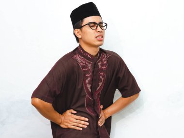 Sağlıksız bir Asyalı Müslüman adamın portresi beyaz arka planda acı içinde karnını tutuyor. İslami yaşam tarzı ve Ramadhan kavramları için mükemmel, dini oruç tutma mücadeleleri.