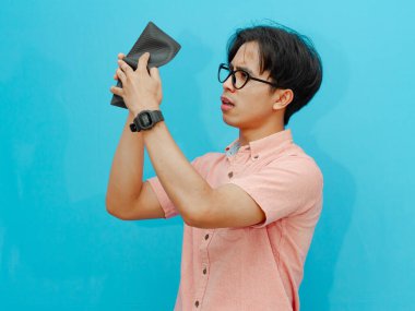 Mavi arka planda cüzdanı olan genç Asyalı bir adam.