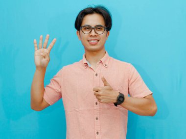 adult Asian man smiling while showing four fingers and giving a thumbs up. Isolated on blue background, suitable for advertising or promotional purposes. clipart