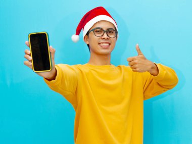 Noel şapkalı mutlu Asyalı adam boş akıllı telefon ekranı gösteriyor..