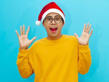 Noel şapkalı heyecanlı genç Asyalı adam kameraya bakarken şaşırmış bir ifade sergiliyor..